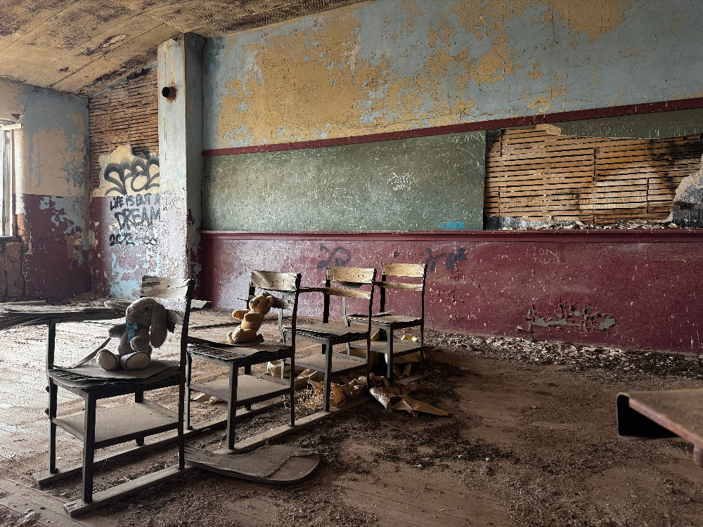 Abandoned classroom with desks and teddy bears, peeling paint, and graffiti.