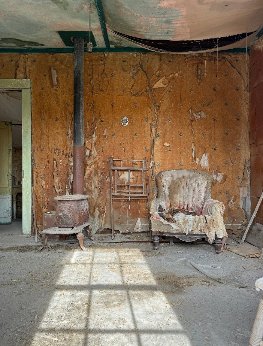 Abandoned room in Bodie, California with an old chair and a stove, walls showing signs of decay and peeling paint.