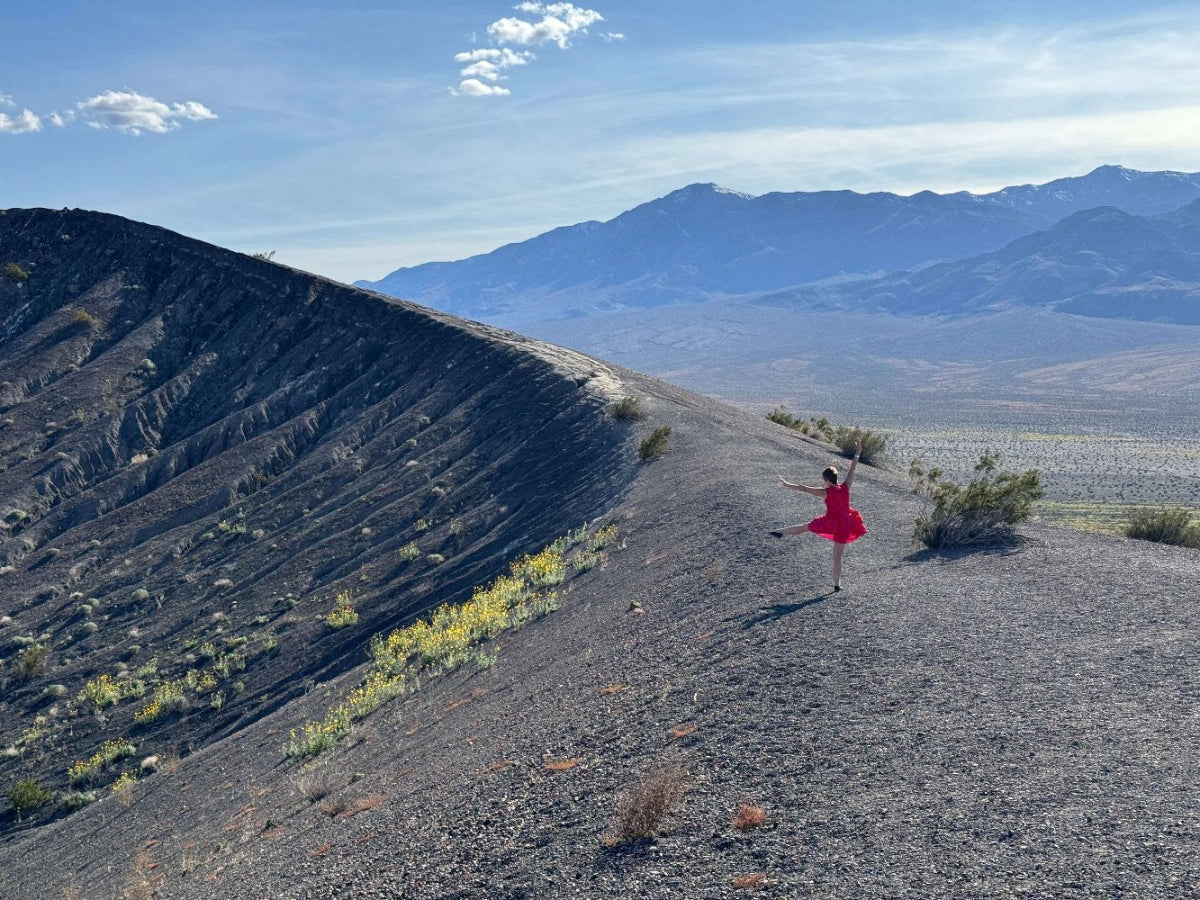 A person in a red dress standing on the rim of Ubehebe Crater with the vast desert landscape and mountains in the background.