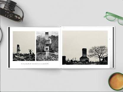 Photobook with black and white images of a tower and trees on a white surface with a camera and glasses.