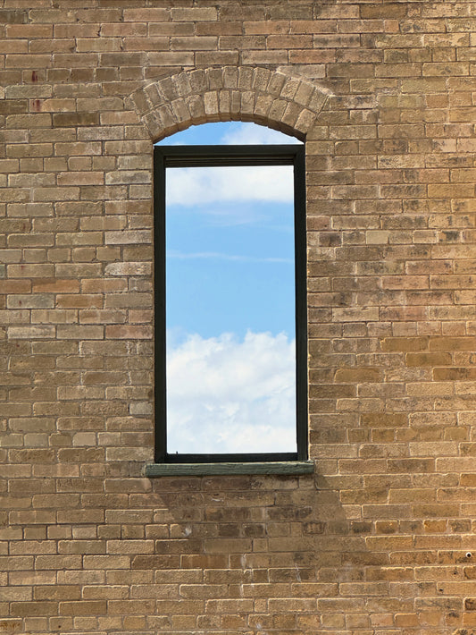 Brick wall with a rectangular window reflecting blue sky and clouds