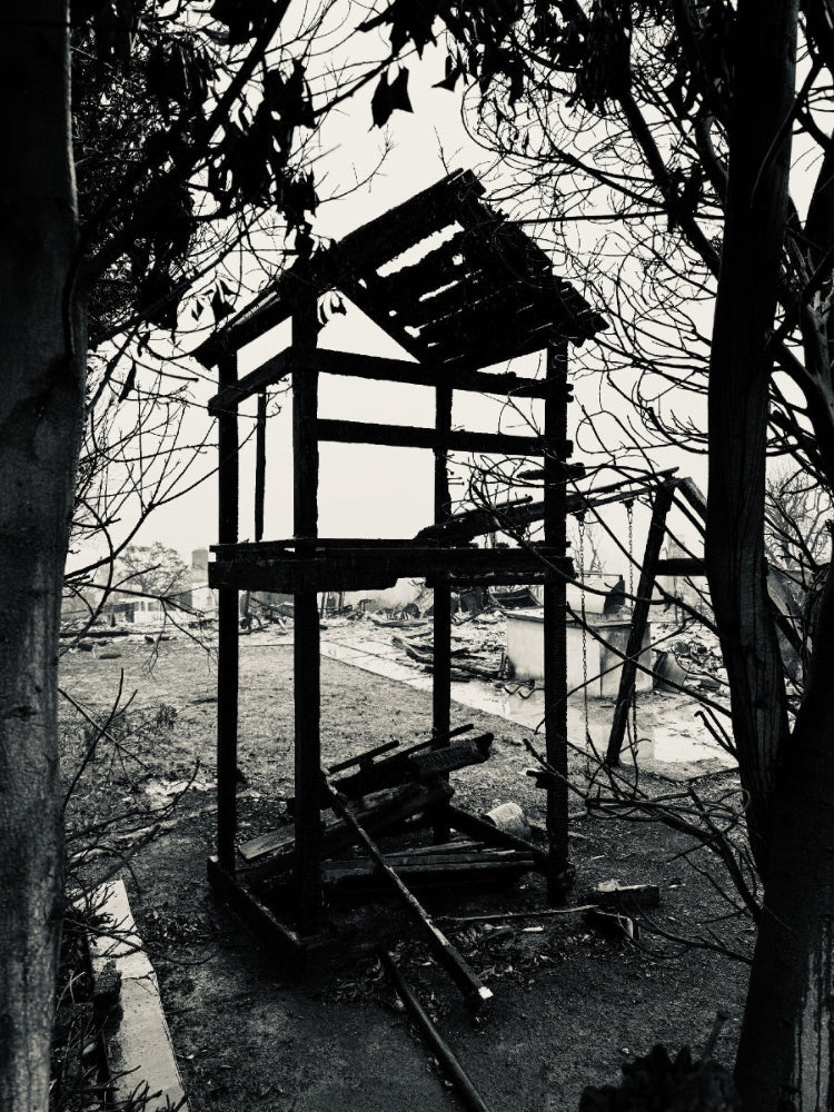Black and white photograph of a dilapidated structure with trees and ruins in the background