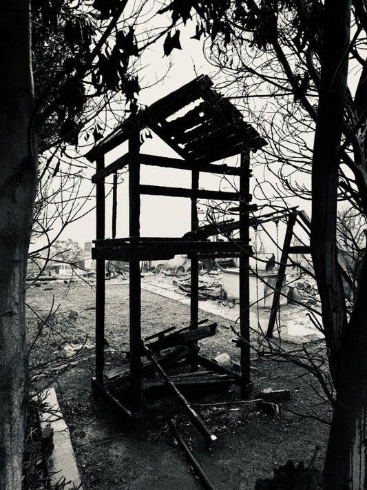 Black and white photograph of a dilapidated structure with trees and ruins in the background