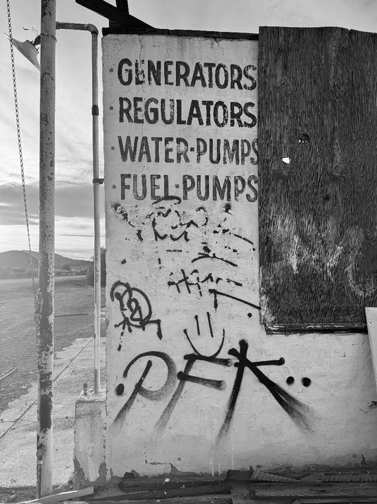 Worn sign with text 'Generators Regulators Water Pumps Fuel Pumps' on a wall with graffiti.