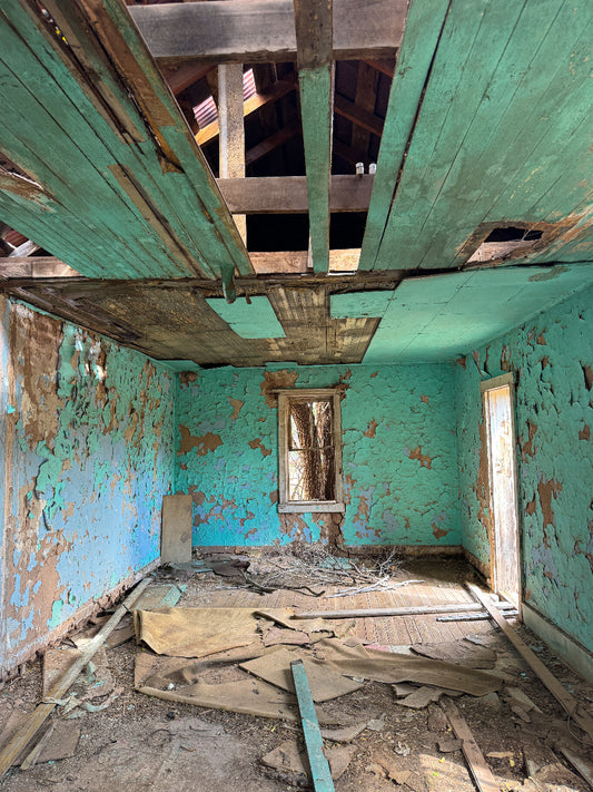 Abandoned room with peeling blue paint on walls and wooden ceiling beams.