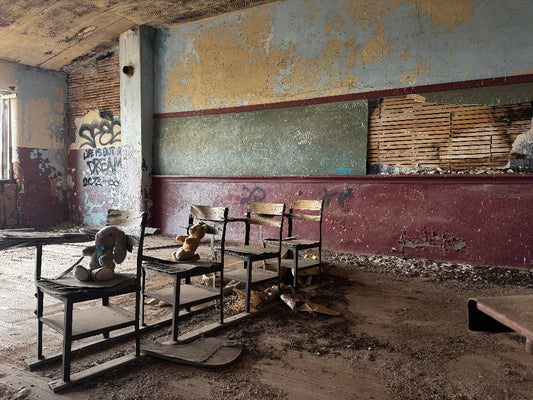Abandoned classroom with desks and teddy bears, peeling paint, and graffiti.